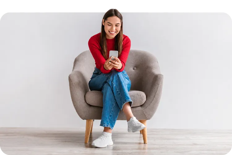Mujer joven sonriendo mientras revisa su teléfono sentada en una silla